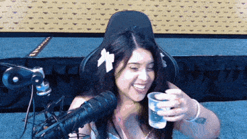 a woman sitting in front of a microphone with a cup of water in her hand