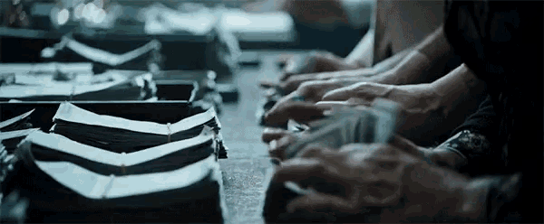 a group of people are sitting at a table with their hands on a stack of money .