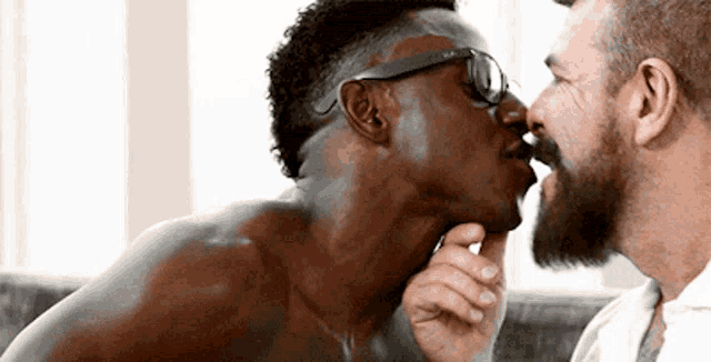 a man with glasses is kissing another man 's neck .