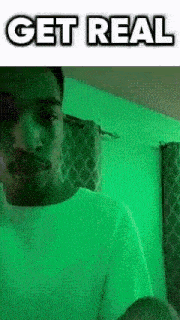 a man in a white shirt is standing in front of a green wall with the words `` get real '' .