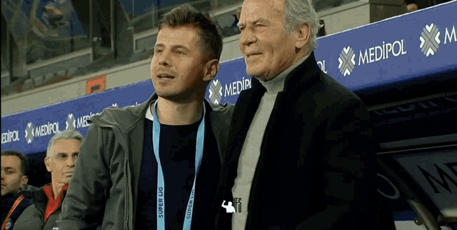 a man wearing a lanyard that says super lig stands next to an older man