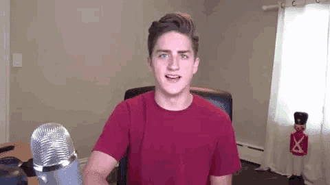 a young man in a red t-shirt is sitting in front of a microphone .