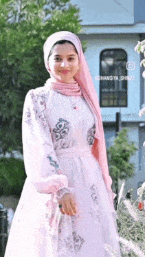 a woman wearing a pink hijab and a white dress is standing in front of a building