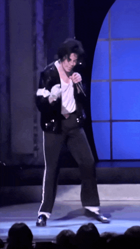 a man in a black jacket is singing into a microphone on a stage