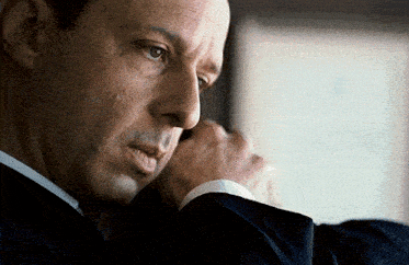 a man in a suit is looking out a window with his hand on his chin