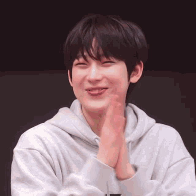 a young man wearing a gray hoodie is smiling and clapping his hands .