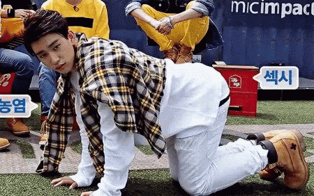 a man in a plaid shirt and white pants is kneeling down on the grass .
