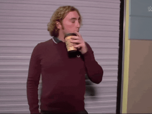 a man in a maroon sweater is drinking from a paper cup