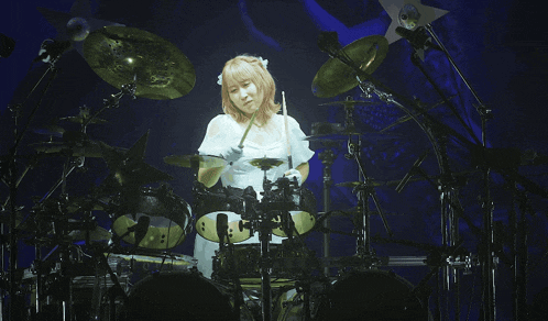 a woman in a white dress is playing drums on stage