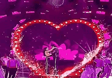 a man and a woman are dancing on a stage in front of a purple heart .