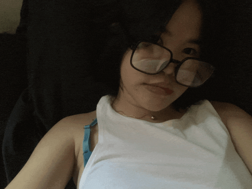 a woman wearing glasses and a white tank top takes a selfie