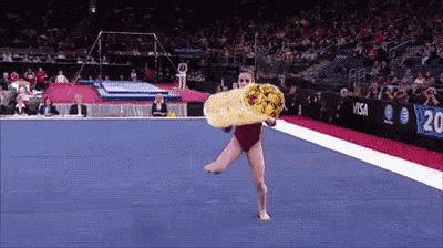 a female gymnast is holding a burrito while doing a trick on the floor