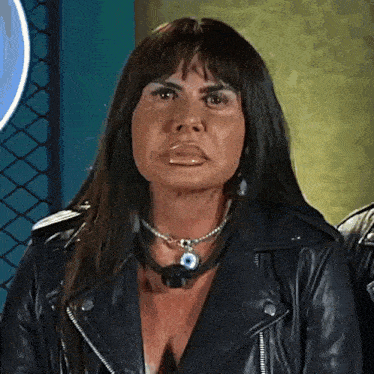 a woman wearing a leather jacket and a necklace is making a face