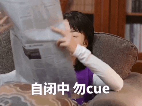 a woman is sitting on a couch reading a newspaper with cue written on the bottom
