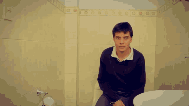 a young man is sitting on a toilet in a bathroom with circles on the wall