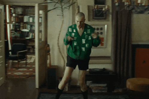 a man in a green sweater and shorts is dancing in a living room