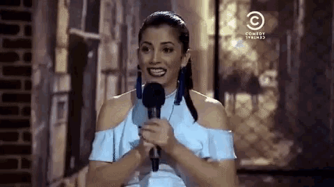 a woman in a blue dress is holding a microphone in front of a comedy central logo
