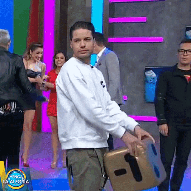 a man in a white sweatshirt is holding a gold cube with the letter t on it