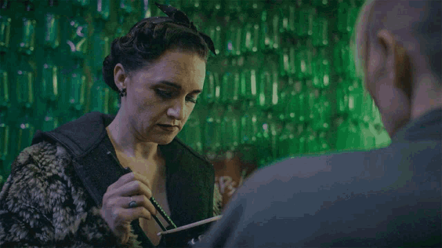 a woman is writing on a piece of paper in front of a green wall that says ' coca cola ' on it