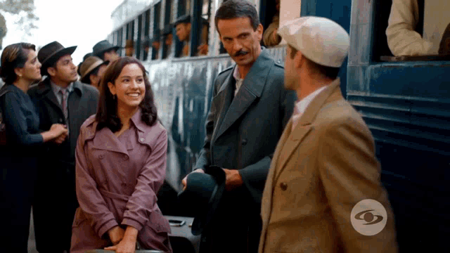 a man in a hat stands next to a woman in a trench coat and a man in a suit