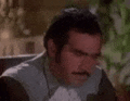 a man with a mustache and a white shirt is looking at the camera .