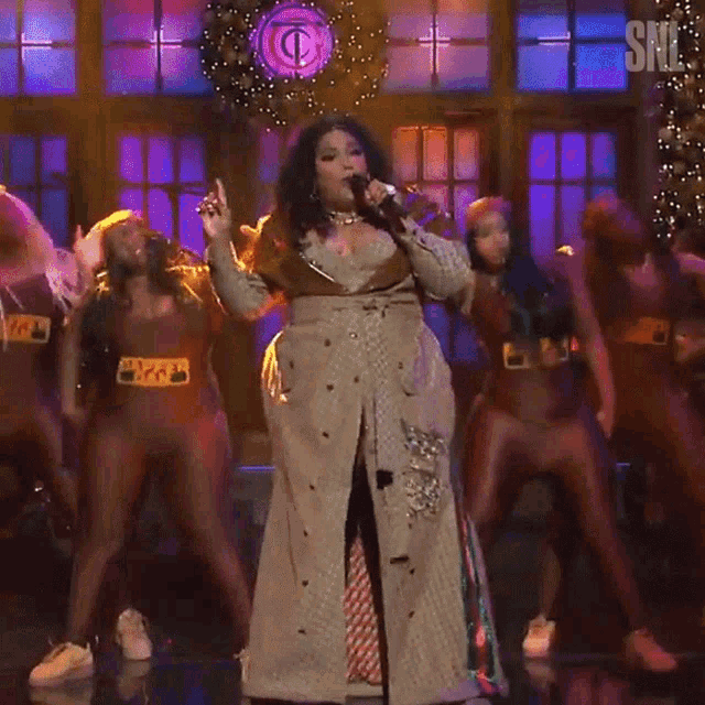 a woman singing into a microphone on a stage with a snl logo behind her