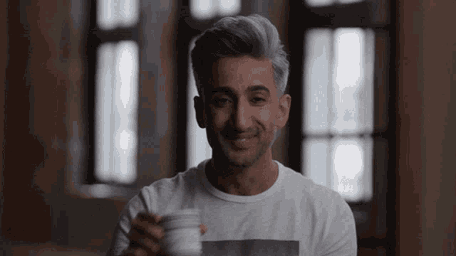 a man in a white shirt is smiling and holding a cup