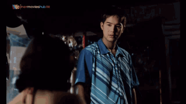 a man in a blue striped shirt is standing in front of a sign that says pinoy movies hub
