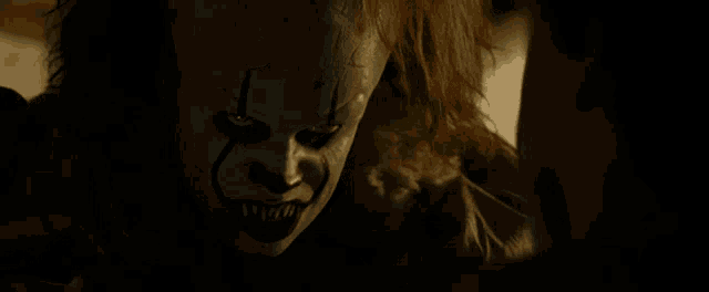 a close up of a scary clown with sharp teeth looking at a person .