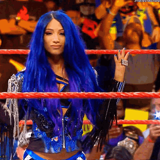 a woman with blue hair is standing in a wrestling ring