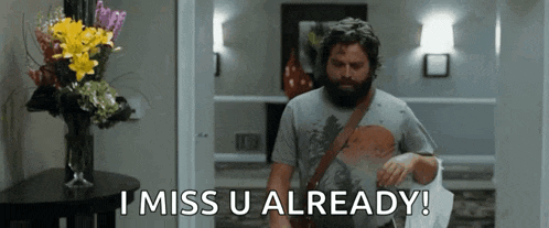 a man with a beard is standing in a hallway and says i miss u already