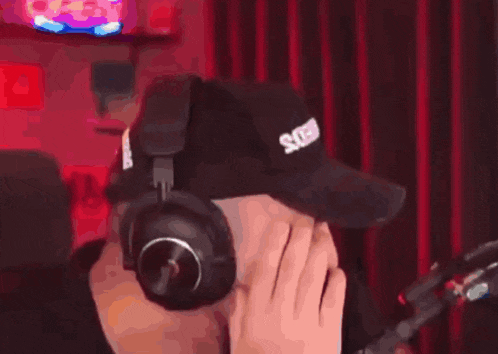 a man wearing headphones and a hat is sitting in front of a microphone covering his face .