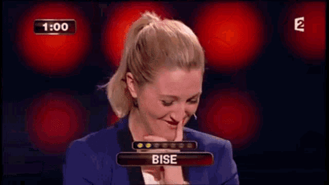 a woman in a blue suit is holding her finger to her lips and the word bise is on the screen behind her