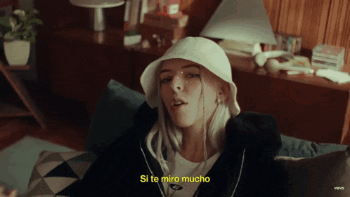 a woman wearing a white hat is sitting on a couch with the words si te miro mucho below her