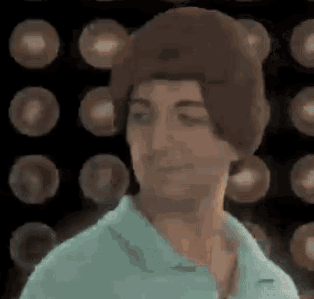 a man wearing a beanie and a blue shirt is standing in front of a bunch of lights .