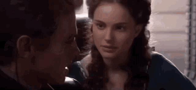 a man and a woman are looking at each other in a room . the woman is wearing a blue dress .