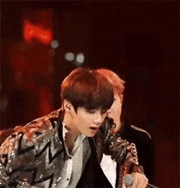 a man in a sequined jacket is singing into a microphone .