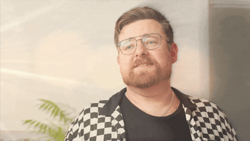 a man with glasses and a beard is wearing a black and white checkered jacket