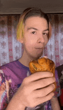 a young man with pink and yellow hair is holding a pastry