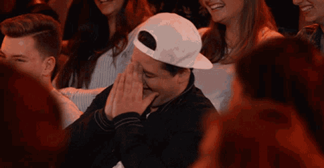 a man wearing a white hat is laughing while sitting in a crowd