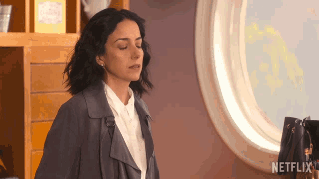 a woman standing in front of a window with a netflix logo on the bottom right