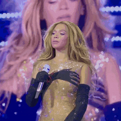 a woman in a gold dress is singing into a microphone while wearing black gloves