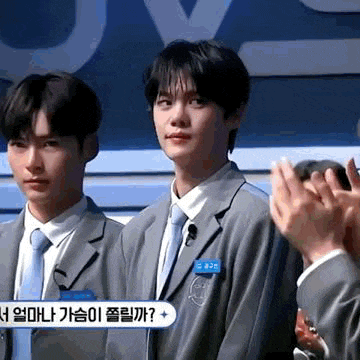 two young men in suits and ties are standing next to each other and applauding .