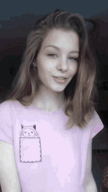 a young woman wearing a pink shirt with a cat in a pocket