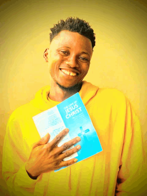 a young man in a yellow hoodie holds a book titled the life of jesus christ