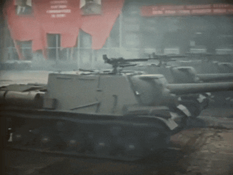 a row of military tanks are parked in front of a building with a red banner that says ' lenin ' on it