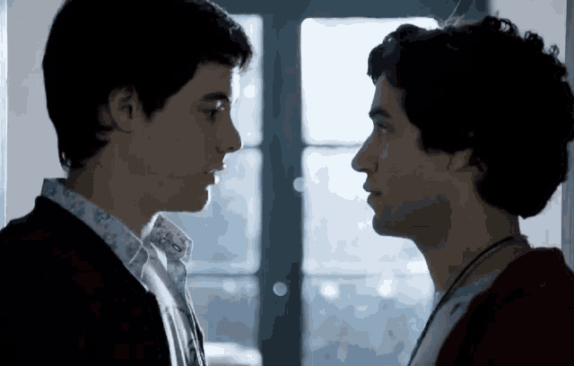 two men are looking at each other with their eyes closed in front of a window