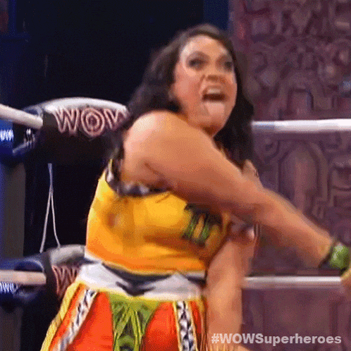 a woman in a yellow top and orange shorts is standing in a wrestling ring and screaming .