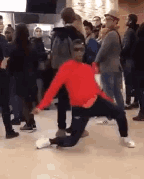 a man in a red jacket is kneeling on the floor in front of a crowd of people .