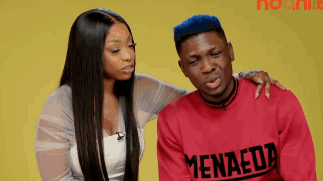 a man wearing a red shirt that says menaeda is sitting next to a woman